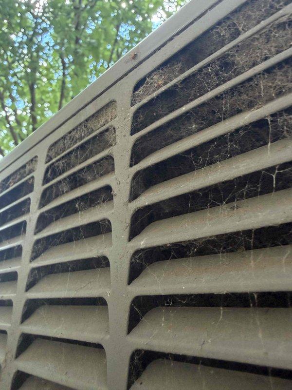 Responded to service call for air conditioning system not cooling adequately. Upon inspection, found outdoor condenser unit with heavily soiled exterior grille, extensive cobweb accumulation, and significant debris buildup restricting airflow. Condenser coil exhibited yellow-green biological growth consistent with mold or algae contamination, along with dirt accumulation between fins. Performed thorough cleaning of condenser coil using approved coil cleaner to remove biological growth and debris. Cleared exterior grille of obstructions and removed accumulated dirt from unit housing. Restored proper airflow through condenser coil by straightening fins and ensuring unobstructed ventilation. System tested and confirmed improved cooling performance following maintenance procedures.