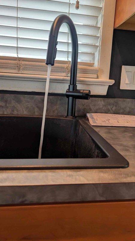 Replaced customer-supplied kitchen faucet with modern pull-down style unit featuring curved spout design and matte black finish. Installed faucet onto undermount sink, ensured proper water flow and spray head functionality, and verified all connections were secure with no leaks detected upon testing.