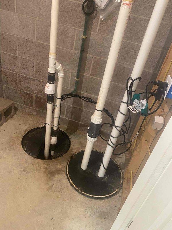 Removed existing battery backup sump pump system and installed new electric-powered unit with 65-watt ampere-hour capacity. Verified proper operation of dual sump pump configuration with PVC discharge piping, check valves, and electrical connections to ensure reliable basement water management and flood protection.