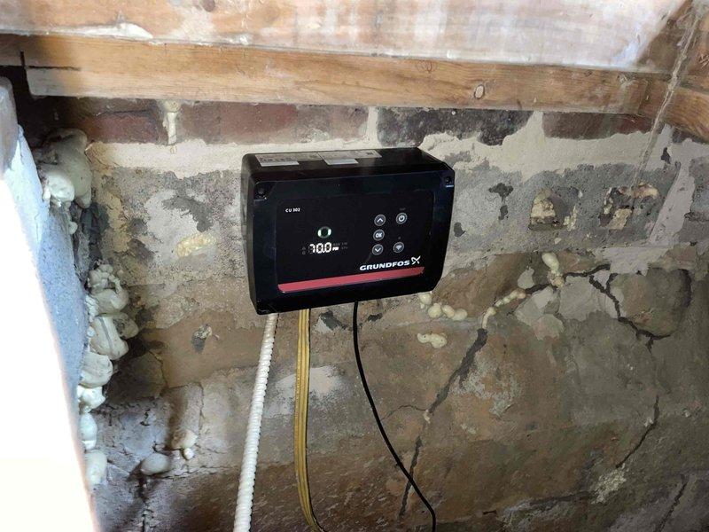Completed follow-up installation of Grundfos constant pressure system in basement location. Installed stainless steel pressure tank with associated piping, pressure gauge, valves, and digital control unit mounted to existing masonry wall. System configured and tested at 100% capacity, with all connections secured using PVC and metal fittings. Control unit programmed and operational, providing automated pressure regulation for residential water supply.