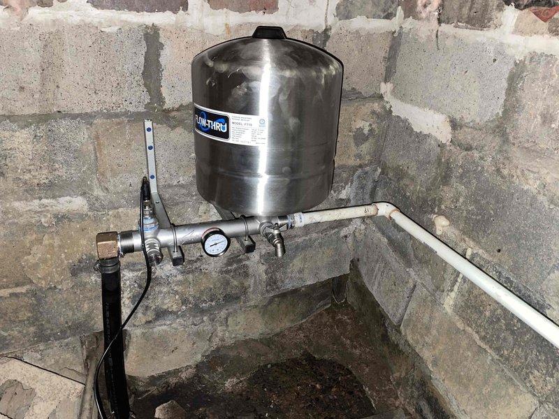 Completed follow-up installation of Grundfos constant pressure system in basement location. Installed stainless steel pressure tank with associated piping, pressure gauge, valves, and digital control unit mounted to existing masonry wall. System configured and tested at 100% capacity, with all connections secured using PVC and metal fittings. Control unit programmed and operational, providing automated pressure regulation for residential water supply.
