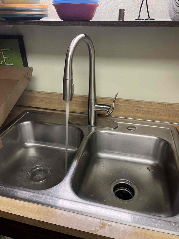 Installed new pull-down kitchen faucet with brushed nickel finish and single-handle operation in double-basin stainless steel sink. Replaced both hot and cold water shut-off valves under sink with new chrome fixtures and connected supply lines to ensure proper water flow and prevent future leaks.