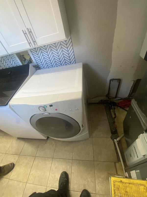 Completed sold repair work in residential laundry and water heater areas. Installed and connected dual water heater system with copper and black steel piping, including multiple shut-off valves with color-coded handles for system control. Configured plumbing connections for washing machine installation with exposed copper supply lines and drainage fittings on tile flooring.