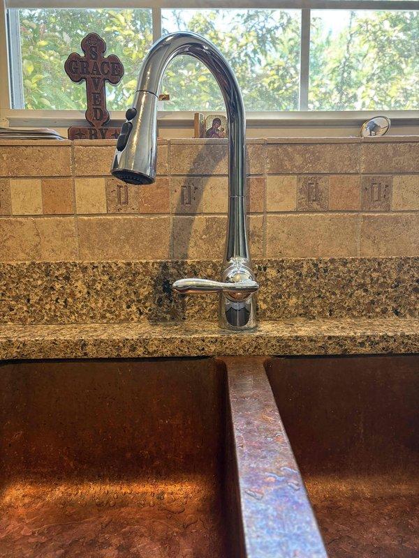 Responded to callback for kitchen sink faucet with insufficient clearance preventing full range of motion from hot to cold positions. Inspected pull-down chrome faucet installation and verified limited swing radius due to positioning constraints. Cleared clogged kitchen sink drain that customer had previously attempted to treat with chemical drain cleaners without success. Confirmed no additional drains were affected. Cleared blockage and restored proper drainage function. Documented under-sink plumbing configuration including braided supply lines, copper piping, and shut-off valves for future reference.