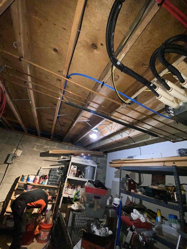 Returned to site to complete installation of new 40-gallon indirect water heater system with two technicians working full day on project. Integrated water heater into existing plumbing infrastructure with new copper piping, compression fittings, and brass connections mounted to basement wall. Installed inline water filtration system with blue housing and black cap, incorporating flow control valve and necessary shut-off components. Routed utility lines through basement ceiling joists, securing black flexible conduit, blue piping, and insulated lines with appropriate fasteners and zip ties. All connections tested and system confirmed operational upon completion of installation.