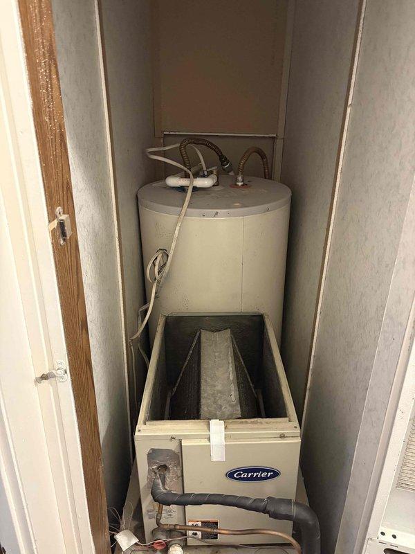 Completed site assessment for full HVAC system replacement in 1500 sq ft mobile home. Evaluated existing Carrier air handler and furnace installation in confined utility closet with water heater. Prepared estimate for replacement of both heating and cooling systems with new 15kW electric furnace and 2.5 ton air conditioning unit. Assessment included evaluation of current vertical stacked configuration, existing ductwork connections, PVC condensate drain lines, and electrical service requirements. Recommended thermostat relocation to optimize placement closer to equipment for improved system control and accessibility.