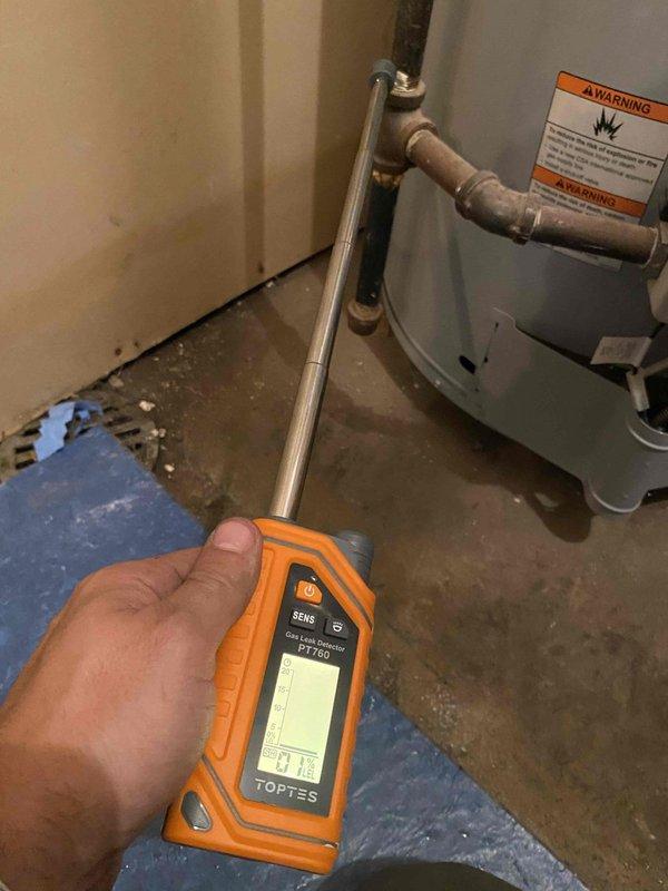 Responded to water leak at boiler/plumbing connection point. Upon arrival, inspected water heater tank base and identified moisture accumulation on concrete floor near copper pipe connections and gas control valve assembly. Utilized diagnostic temperature probe to assess system conditions and verify leak source at the interface between plumbing lines and water heater unit. Documented equipment condition including gas control valve assembly, copper piping connections, and warning labels for service records.