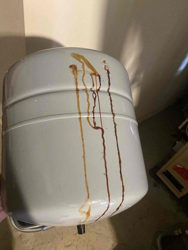 Responded to service call for a 6-year-old boiler system with a leaking expansion tank. Upon inspection, found the Amtrol expansion tank actively leaking, causing water damage and rust-colored staining on the adjacent water heater tank. Documented the leak and resulting corrosion with photographs. Recommended immediate replacement of the failed expansion tank to prevent further water damage and maintain proper system pressure. Customer approved replacement work.