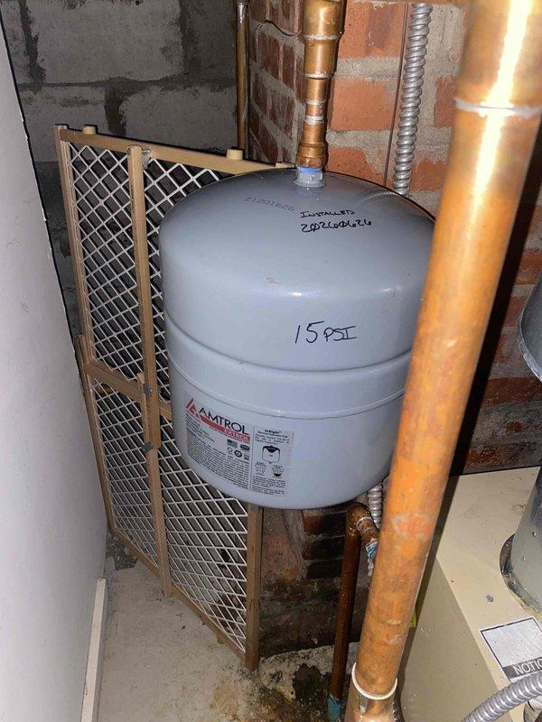 Responded to service call for a 6-year-old boiler system with a leaking expansion tank. Upon inspection, found the Amtrol expansion tank actively leaking, causing water damage and rust-colored staining on the adjacent water heater tank. Documented the leak and resulting corrosion with photographs. Recommended immediate replacement of the failed expansion tank to prevent further water damage and maintain proper system pressure. Customer approved replacement work.