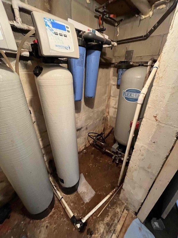 Responded to warranty service call for no water condition at property with well pump system installed approximately two years prior. Upon arrival, conducted comprehensive diagnostic assessment of water delivery system including well pump operation, pressure tank functionality, and water treatment equipment. 

Inspection revealed issues affecting water flow through the whole-house filtration system located in basement utility area. System consists of multiple treatment tanks including water softener and filtration units with electronic control head. Observed significant moisture accumulation and water staining on concrete floor surrounding treatment equipment, indicating previous leak or drainage concerns. 

Evaluated well pump electrical connections, pressure switch settings, and tank air charge. Tested system components including blue filter housings and verified proper operation of control panel. Assessed all plumbing connections, copper and plastic piping throughout water treatment 