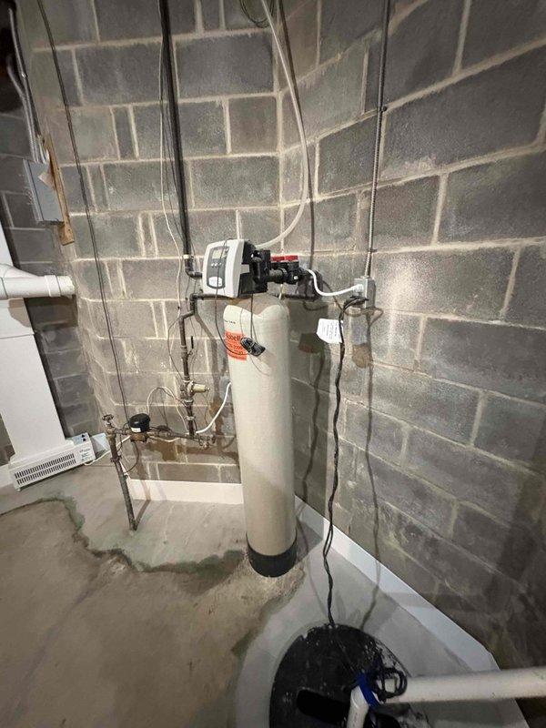 Completed plumbing maintenance inspection at club facility with confirmed tankless water heater system present. Documented basement mechanical room conditions including water softener/filtration unit, associated copper and PVC piping connections, and HVAC heat exchanger components showing normal operational wear and minor surface corrosion. All equipment photographed for maintenance records.