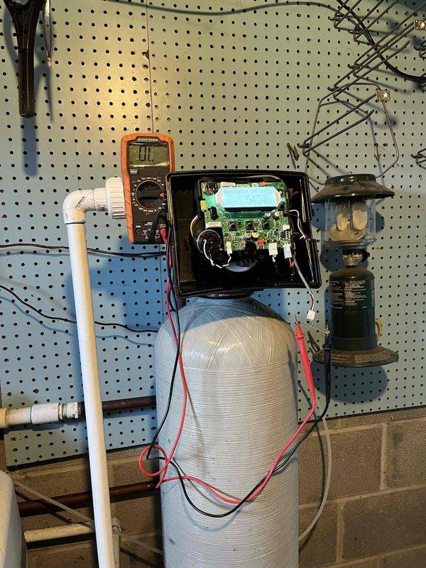 Responded to service call for non-operational Stenner chemical feed pump with no power indicator light. Upon arrival, performed diagnostic testing using digital multimeter to check electrical components and circuit board functionality. Removed pump housing cover to access internal electronics and identified power supply issue. Tested voltage levels at various connection points on the green circuit board to isolate the electrical fault. Inspected the complete water treatment system installation including blue filter housing, copper piping, pressure gauge, and associated electrical control components to ensure proper integration with the chemical feed pump. Verified all plumbing connections and electrical wiring from the control box to the pump unit were secure and properly terminated. Completed troubleshooting and testing procedures to restore pump operation and system functionality.