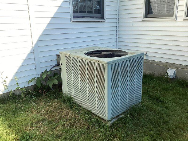 Conducted comprehensive HVAC system assessment for equipment replacement estimate at residential property. Evaluated existing outdoor air conditioning condenser unit with beige/tan metal grille housing and existing wall-mounted programmable thermostat. Documented current system configuration, operational status, and equipment specifications through detailed photography of both outdoor condensing unit and indoor temperature control components to provide accurate replacement recommendations and system sizing requirements.