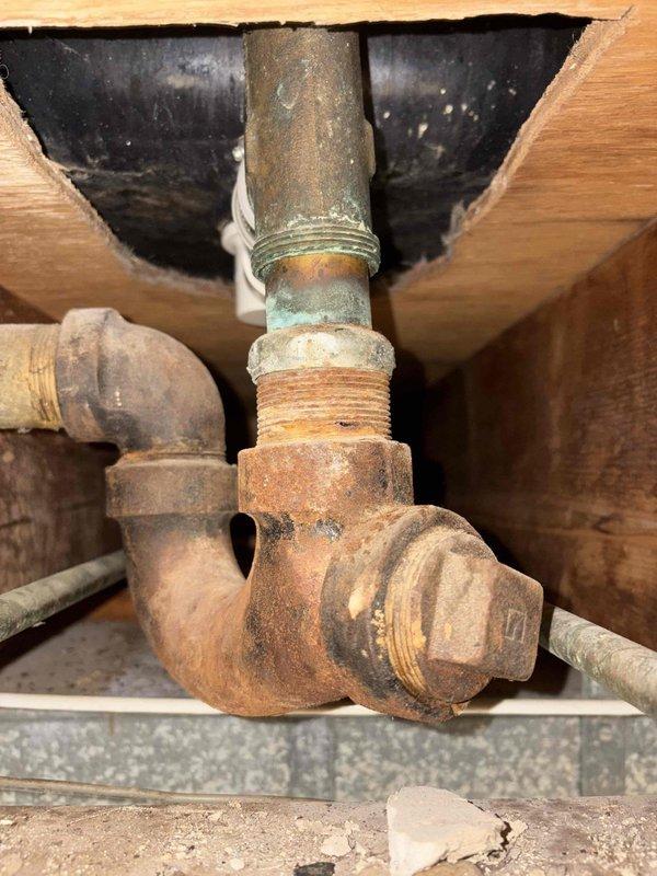 Performed comprehensive plumbing assessment of bathtub drainage system experiencing code violations and active water leakage into basement. Inspection revealed severely corroded cast iron waste piping with compromised threaded connections and deteriorated elbow fittings exhibiting advanced oxidation throughout the drain assembly. Documented existing illegal plumbing configuration preventing proper drainage, including improperly installed PVC transition connections with inadequate rubber couplings in ceiling cavity. Provided detailed photographic documentation of corroded metallic piping requiring complete replacement and recommended full remediation of non-compliant drainage system to restore proper function and prevent continued water damage to basement area.
