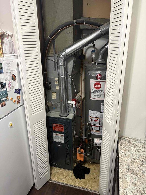 Performed equipment evaluation and replacement estimate for aging HVAC system approximately 27 years old installed in utility closet. Assessed existing American Standard furnace with Kobella service history and adjacent water heater, both showing signs of age-related wear. Documented current equipment configuration including metallic ductwork, flexible ducting connections, copper piping, and circulation pump installation. Provided comprehensive replacement recommendations based on equipment age, efficiency considerations, and customer's expressed interest in system upgrade following previous consultation.