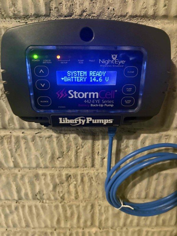Replaced battery in Liberty Pumps StormCell 442-EYE Series battery backup pump control unit. System tested and verified operational with battery voltage reading 14.6V and display showing "SYSTEM READY" status.