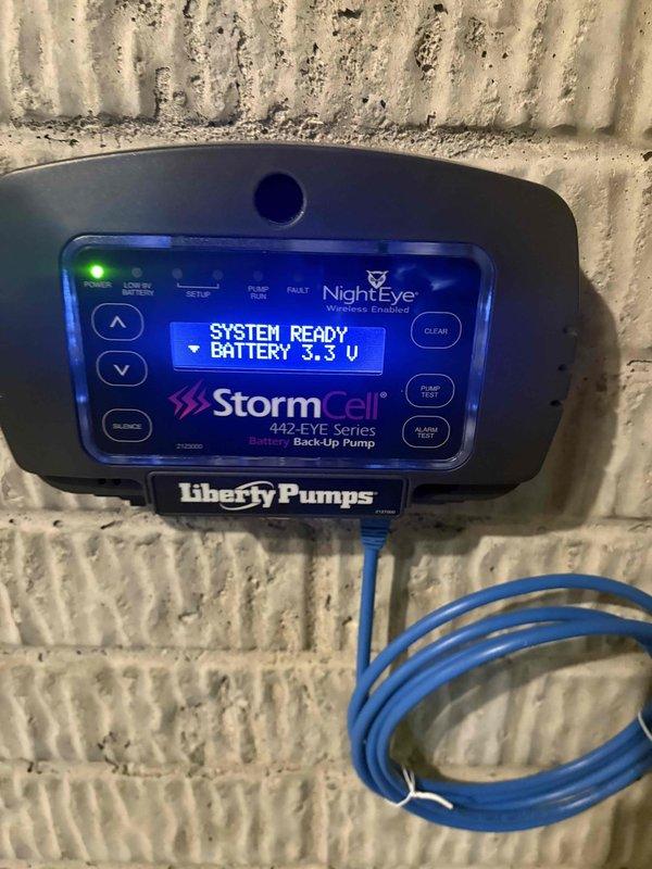 Replaced battery in Liberty Pumps StormCell 442-EYE Series battery backup pump control unit. System tested and verified operational with battery voltage reading 14.6V and display showing "SYSTEM READY" status.