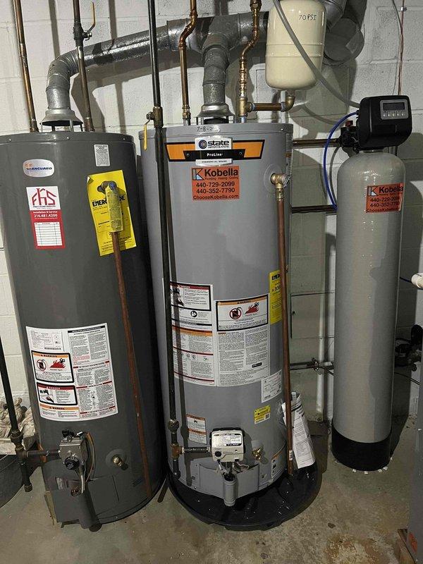 Responded to service call for dual water heater system where one unit's pilot light would not ignite, displaying thermopile low voltage error code upon attempted ignition. Diagnosed failed thermopile preventing pilot assembly from maintaining flame. Coordinated with warranty provider who approved tank replacement with customer responsible for two modifications (waterline and flue) and four code upgrades (shut-off valve, drain pan, T&P drain line, and expansion tank) per plan agreement exclusions. Documented existing State brand water heater installation with copper supply lines, expansion tank, and water treatment system. Photographed burner assembly showing proper blue flame characteristics on operational unit for comparison. Awaiting warranty coverage confirmation on replacement unit cost before proceeding with installation.
