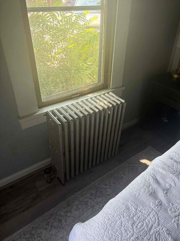 Returned to complete installation of new radiator shut-off valves in Unit 3 following material delivery. Installed brass quarter-turn shut-off valves with compression fittings at the base of white column-style cast-iron radiators in bedroom. Verified proper valve operation and connection integrity to existing plumbing infrastructure.