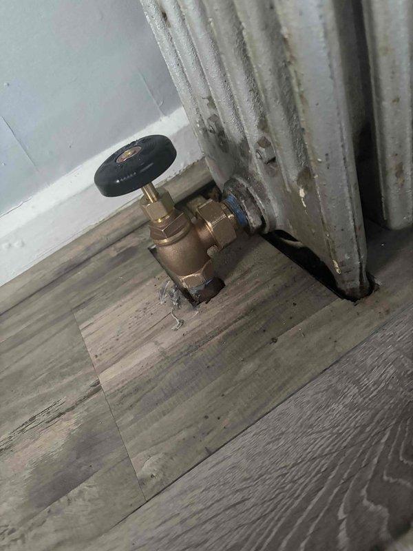 Returned to complete installation of new radiator shut-off valves in Unit 3 following material delivery. Installed brass quarter-turn shut-off valves with compression fittings at the base of white column-style cast-iron radiators in bedroom. Verified proper valve operation and connection integrity to existing plumbing infrastructure.