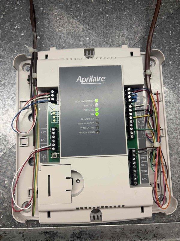 Responded to no cooling call with thermostat display failure. Upon arrival, found Aprilaire control unit with blank display despite hardwired power connection. Inspected control board and wiring connections, verified multiple LED indicators illuminated on circuit board, and assessed internal components including terminal blocks, fuses, and 120V igniter circuit. Documented system configuration and wiring arrangement for HVAC control system diagnostics.