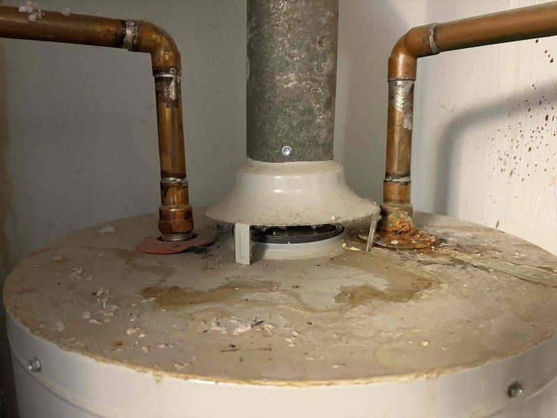 Responded to service call for inoperative gas-fired water heater. Upon arrival, inspected existing unit and confirmed lack of hot water production. Evaluated 40-gallon gas water heater showing significant age-related deterioration, including heavy dust accumulation, water staining on tank exterior, and corrosion visible on copper supply piping connections. Assessed gas control valve, flue venting system, and all associated plumbing connections. Documented existing conditions with photographs showing corroded pipe fittings, mineral deposits, and overall system wear consistent with end-of-service-life failure.