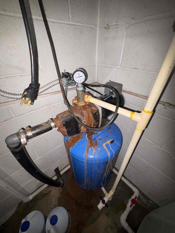 Responded to low water pressure service call and identified multiple critical issues affecting system performance. Well pump failed to shut off due to malfunctioning pressure control system. Discovered significant leak in water filtration tank, evidenced by extensive rust and corrosion on top cap and fittings with visible moisture on floor. Stenner chemical feed pump found to be non-operational. Additionally located active leak in vicinity of water heater. Documented all equipment conditions with photographs showing corroded blue filtration tank with compromised seals and damaged Stenner pump assembly with serial number recorded. Recommended immediate repairs to pressure switch, tank replacement due to severe corrosion compromising structural integrity, Stenner pump repair or replacement, and water heater connection repair to restore proper system function and prevent further water damage.