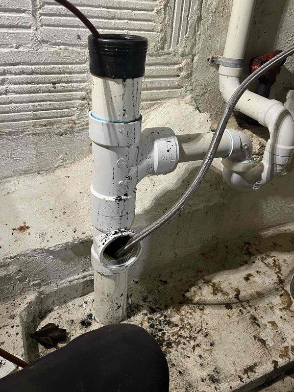 Responded to a main drain cleanout service call for suspected root intrusion in the drainage system. Successfully cleared the blockage from the main sewer line cleanout access point, which had previously required service for similar issues. Removed debris and restored proper drainage flow through the system. The cleanout assembly, located at floor level with PVC piping connections, was accessed and thoroughly cleared using professional drain cleaning equipment. Post-service inspection confirmed full restoration of drainage capacity with no standing water or backup conditions remaining.