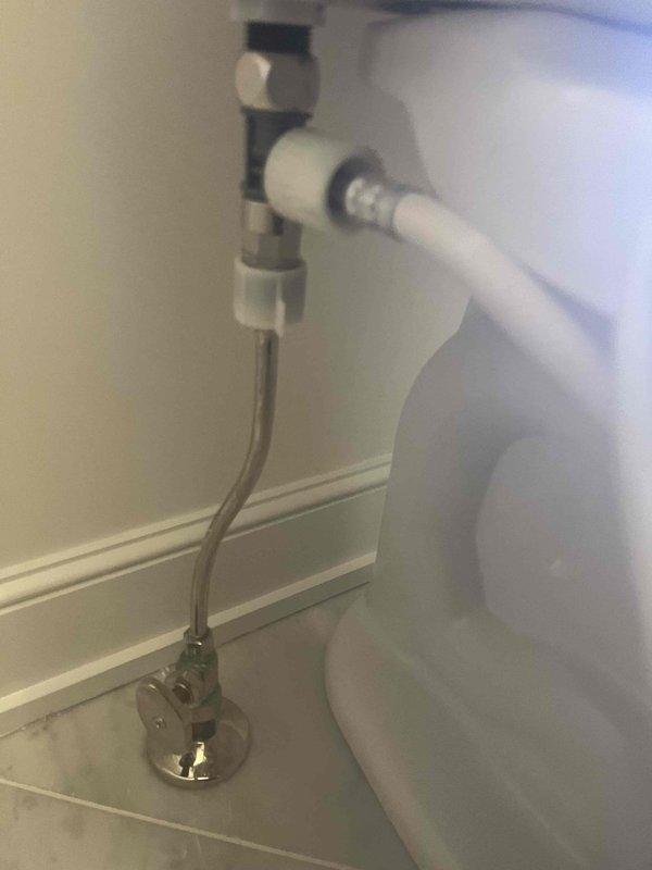Responded to emergency water leak call for residential plumbing system approximately six years old. Upon inspection, identified significant corrosion and verdigris buildup on toilet water supply angle stop valve and connecting components, with visible rust discoloration on internal valve components. The corroded valve assembly posed an active leak risk and required immediate attention. Documented existing conditions showing deteriorated chrome-plated fixtures with green oxidation on threaded connections and valve body. Assessed flexible braided stainless steel supply line connection from wall-mounted angle stop to toilet tank inlet. All findings were photographed for service records, capturing the corroded valve assembly and complete toilet supply line installation to document the source of the water leak concern.