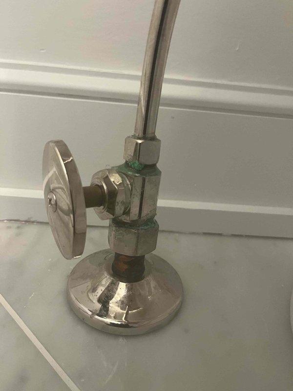 Responded to emergency water leak call for residential plumbing system approximately six years old. Upon inspection, identified significant corrosion and verdigris buildup on toilet water supply angle stop valve and connecting components, with visible rust discoloration on internal valve components. The corroded valve assembly posed an active leak risk and required immediate attention. Documented existing conditions showing deteriorated chrome-plated fixtures with green oxidation on threaded connections and valve body. Assessed flexible braided stainless steel supply line connection from wall-mounted angle stop to toilet tank inlet. All findings were photographed for service records, capturing the corroded valve assembly and complete toilet supply line installation to document the source of the water leak concern.