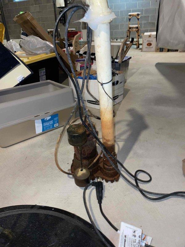 Responded to complaint of loud drilling sound originating from well and water filtration system. Upon inspection, identified severely corroded pump assembly at base of water treatment system as source of noise. The extensive rust on the mechanical components indicated prolonged moisture exposure and equipment failure, causing abnormal operational sounds and compromising system performance. Documented existing conditions showing deteriorated pump unit with connected hoses and electrical components, as well as overall basement water treatment infrastructure including sump pump, drainage system, and filtration equipment for assessment and recommended replacement of failed components.