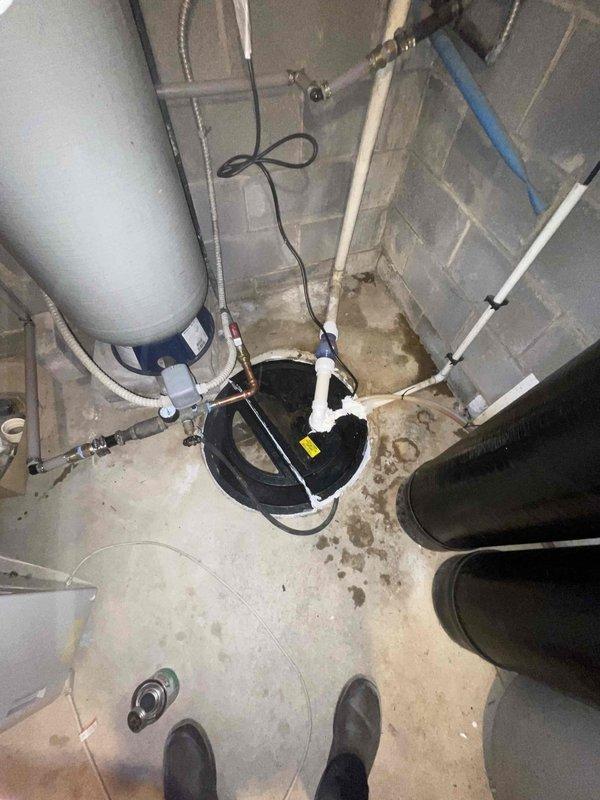 Responded to complaint of loud drilling sound originating from well and water filtration system. Upon inspection, identified severely corroded pump assembly at base of water treatment system as source of noise. The extensive rust on the mechanical components indicated prolonged moisture exposure and equipment failure, causing abnormal operational sounds and compromising system performance. Documented existing conditions showing deteriorated pump unit with connected hoses and electrical components, as well as overall basement water treatment infrastructure including sump pump, drainage system, and filtration equipment for assessment and recommended replacement of failed components.