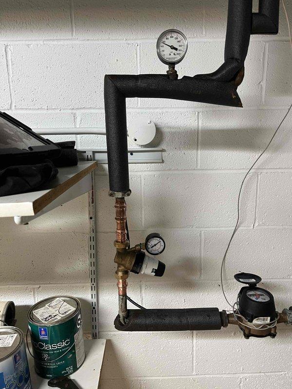 Responded to water leak call near the main water line. Upon arrival, tested system pressure which measured at 80 PSI. Inspected the water main assembly including pressure regulators, shut-off valves, and associated piping. Identified small leak at connection point near the main water supply. Documented existing plumbing configuration including black iron pipe, copper connections, pressure gauges, and flow meter. Also documented 100-gallon natural gas water heater specifications for reference. Repaired leak and verified system integrity upon completion.