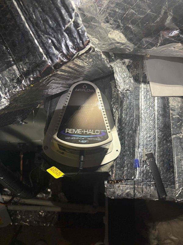 Completed warranty return visit to install REME HALO air purification system on existing HVAC unit in attic space. Cut access hole in sheet metal ductwork to accommodate purification unit installation, mounted device to supply plenum with proper airflow orientation, and connected electrical wiring to complete integration with air handler system.