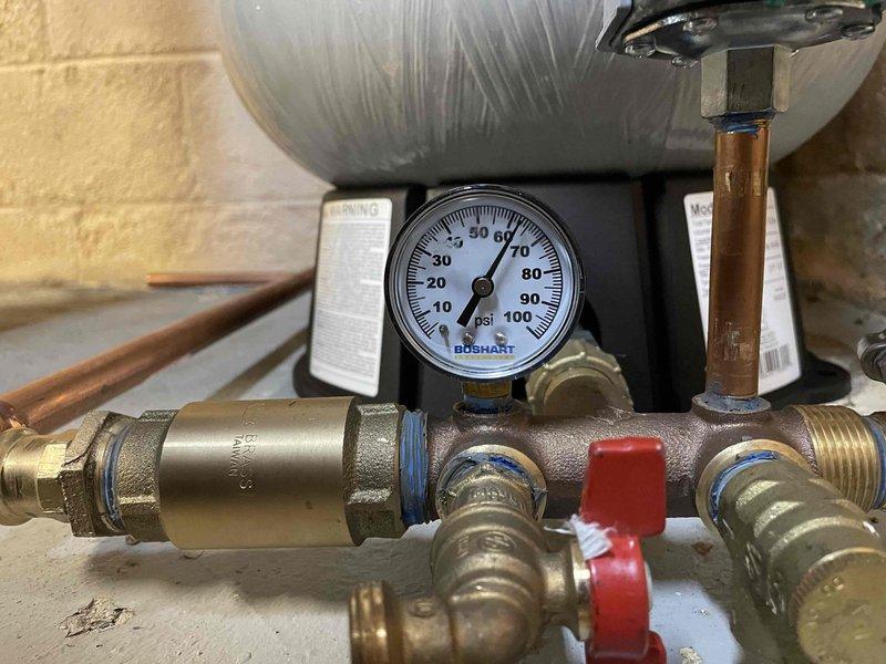 Responded to water leak on well line servicing residential property. Upon inspection, located leak in water supply system and performed necessary repairs to stop water loss. Inspected pressure regulation system including Boshart pressure gauge and brass manifold assembly with red-handled isolation valve. Verified proper operation of pressure regulator and associated copper piping connections. Checked water heater installation and gas valve assembly for any related issues or water damage. Completed repairs to well line, restored water service, and confirmed system pressure within normal operating parameters. All connections tested and verified leak-free upon completion.