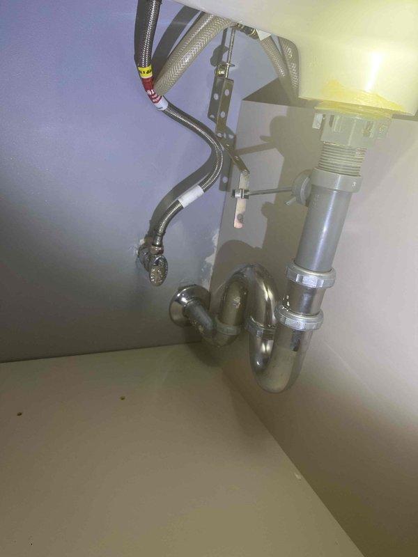 Completed plumbing estimate for basement piping replacement project. Assessed multiple corroded shut-off valves with blue handles installed on copper water supply lines beneath floor joists, noting extensive condensation on existing foam pipe insulation throughout the system. Evaluated deteriorated S-traps and sink drain assemblies requiring replacement, including chrome-finished P-trap configuration with vertical drain connections and braided stainless steel supply lines mounted to wall surface. Documented current conditions of plumbing fixtures, pipe fittings, and drainage components to provide accurate replacement recommendations for corroded valves and trap assemblies.