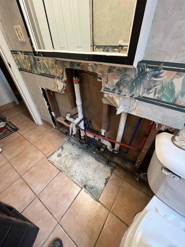 Responded to emergency service call for pipe burst with water supply shut off. Conducted comprehensive assessment of damaged plumbing system to prepare insurance claim estimate. 

Inspected corroded copper piping in basement utility area showing extensive green patina (verdigris) and oxidation damage throughout multiple sections. Documented deteriorated pipe assembly including galvanized steel elbow fitting, metal coupling bands, and connection points exhibiting significant age-related degradation from prolonged moisture exposure. Evaluated structural integrity of affected copper lines and adjacent plumbing components.

Assessed bathroom vanity area where demolition work exposed wall cavity and plumbing infrastructure. Examined white PVC drain lines, red and blue PEX supply tubing, and gray piping running through wall studs. Documented existing plumbing configuration and water damage extent for estimate preparation. Photographed all affected areas including exposed framing, pipe routin