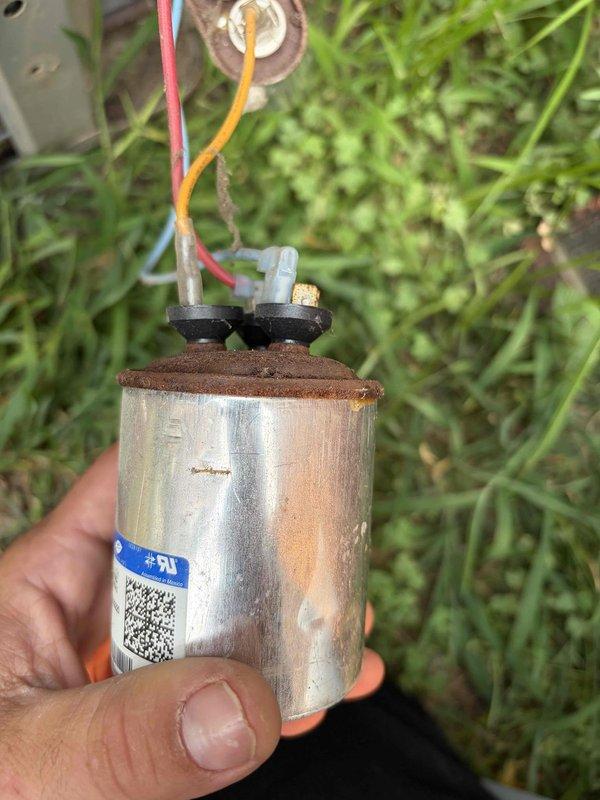 Responded to no-cool call on residential air conditioning system of unknown age. Upon inspection, found failed dual run capacitor with severe rust and corrosion on terminal connections. Capacitor showed signs of extended exposure to moisture and environmental degradation, causing complete system shutdown. Removed defective capacitor and installed new replacement unit with proper electrical connections. Verified all wire terminations were secure and tested system operation. Unit successfully powered on with compressor and condenser fan motor running properly. System returned to normal cooling operation.