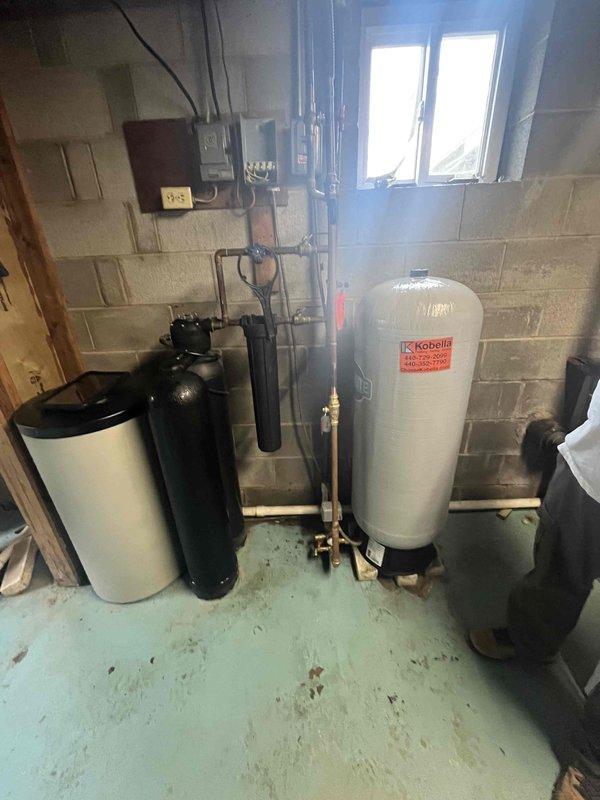 Completed water heater replacement in basement of older residential property. Existing water heating system was removed and new unit installed, integrated with existing plumbing infrastructure including water softener, filtration system, and pressure tank. All copper pipe connections, valves, and fittings were properly configured to ensure seamless operation with the home's water treatment equipment.