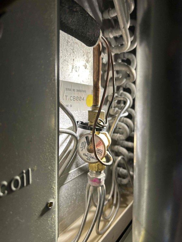 Responded to no cooling call at vacant property for 2009 Goodman system. Upon arrival, verified ambient temperature reading of 75.1°F and inspected outdoor condensing unit. Observed refrigerant lines, brass service valves, and system components showing age-related wear consistent with 10+ year old equipment, with service port tape indicating previous refrigerant work.