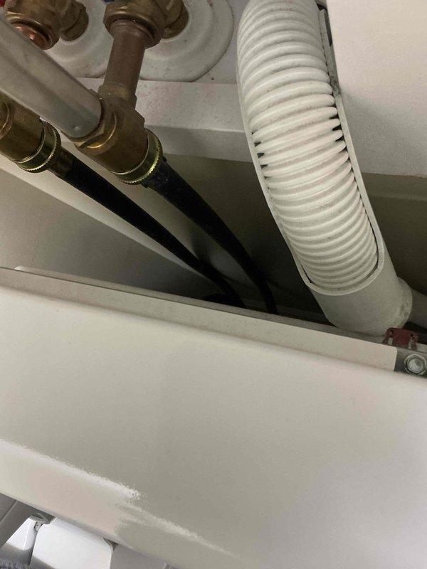 Completed routine plumbing maintenance inspection under sink fixture. Documented existing plumbing configuration including brass compression valve fittings, flexible supply lines, and white corrugated drain/vent hose, confirming all components are properly connected and functional with normal age-appropriate wear on brass fittings.