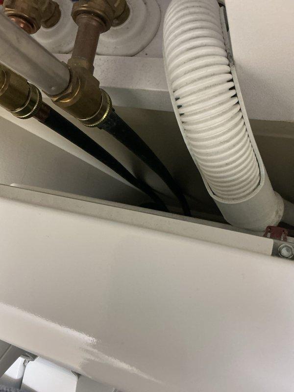 Completed routine plumbing maintenance inspection under sink fixture. Documented existing plumbing configuration including brass compression valve fittings, flexible supply lines, and white corrugated drain/vent hose, confirming all components are properly connected and functional with normal age-appropriate wear on brass fittings.