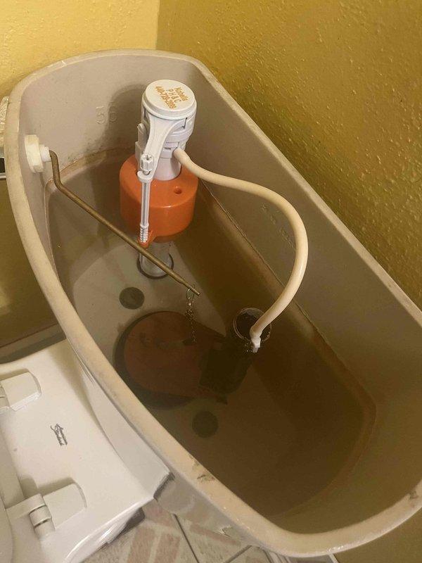 Completed follow-up plumbing service for previously sold jetting work. Inspected toilet flange installation in tiled bathroom floor and examined internal tank components including fill valve with float assembly and overflow tube connection. Documented existing conditions showing worn flooring around fixture and mineral staining in tank interior to verify system functionality after jetting service.
