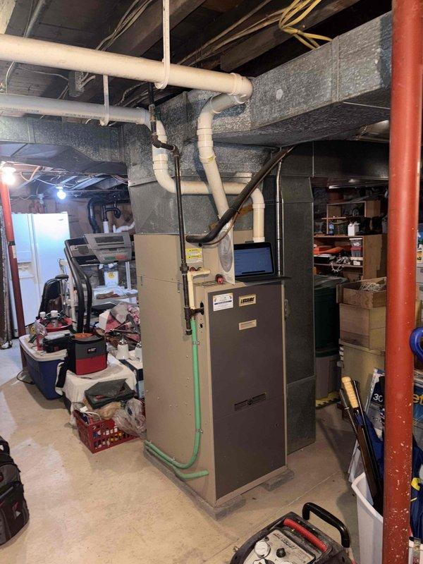 Conducted replacement estimate for residential HVAC system with 25-year-old Lennox furnace located in basement and matching-age outdoor air conditioning condenser unit. Both systems have exceeded their typical service life expectancy and are candidates for complete replacement with modern, energy-efficient equipment. Documented existing equipment conditions through photographs showing outdoor condenser unit on concrete pad with weathered foundation surroundings and basement furnace installation with current ductwork, refrigerant lines, and PVC venting configuration.