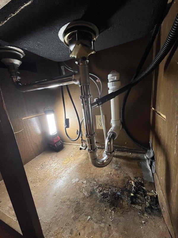 Responded to service call for drain clearing, faucet replacement, and air admittance valve installation at kitchen sink. Upon arrival, found evidence of previous drainage issues with visible water damage and debris accumulation on cabinet floor beneath sink. Successfully cleared blocked drain line using appropriate drain cleaning equipment. Removed existing faucet assembly and installed new replacement unit, ensuring proper connections and testing for leaks. Added air admittance valve to plumbing system to address venting requirements and prevent future drainage problems. Verified all plumbing connections were secure, tested water flow and drainage functionality, and confirmed no leaks present upon completion.
