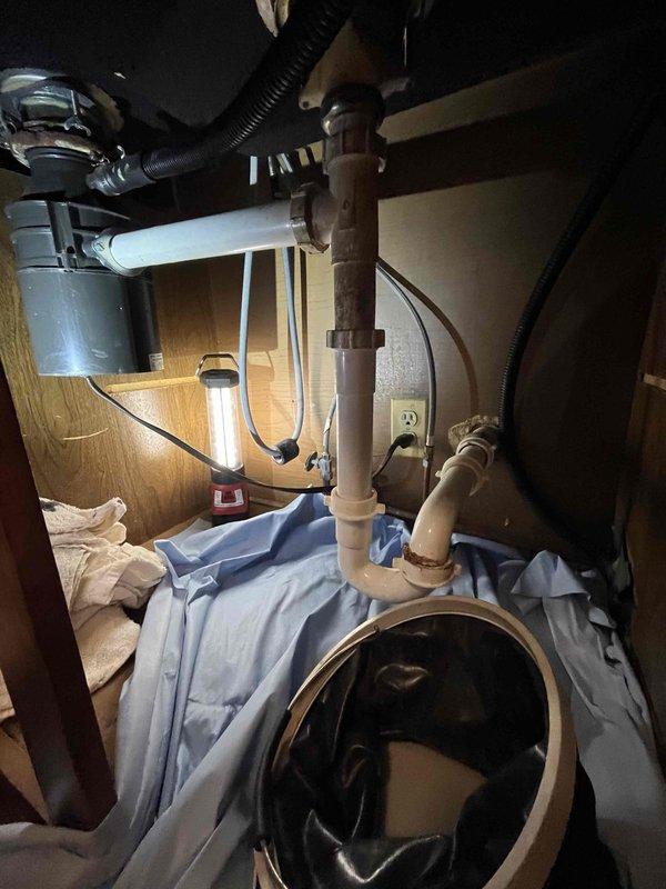 Responded to service call for drain clearing, faucet replacement, and air admittance valve installation at kitchen sink. Upon arrival, found evidence of previous drainage issues with visible water damage and debris accumulation on cabinet floor beneath sink. Successfully cleared blocked drain line using appropriate drain cleaning equipment. Removed existing faucet assembly and installed new replacement unit, ensuring proper connections and testing for leaks. Added air admittance valve to plumbing system to address venting requirements and prevent future drainage problems. Verified all plumbing connections were secure, tested water flow and drainage functionality, and confirmed no leaks present upon completion.