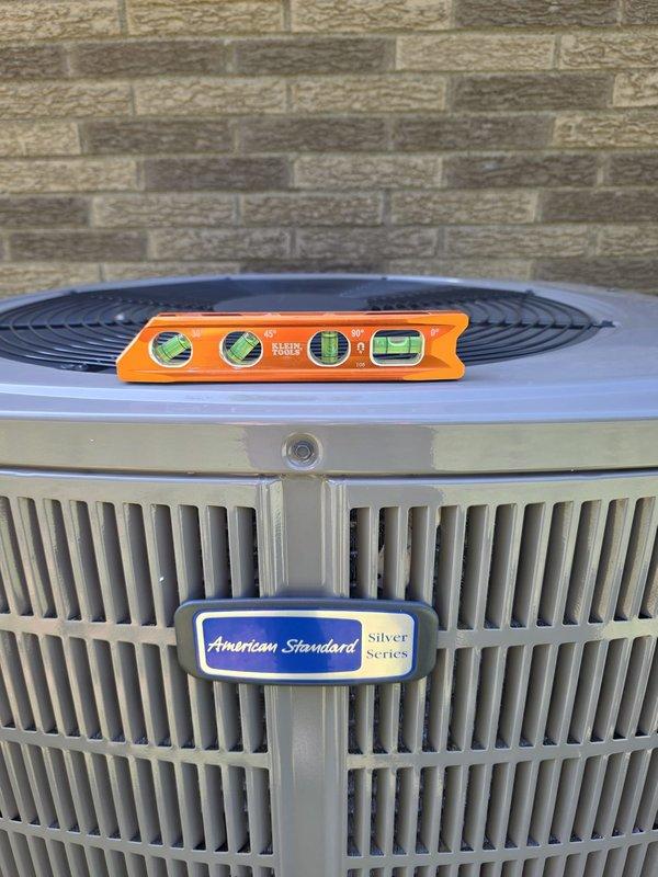 Completed full HVAC system installation including outdoor American Standard Silver Series condenser unit positioned and leveled against exterior brick wall with protective top cover installed. Interior work included installation of new filter-drier assembly with proper copper line connections, routing of flexible ductwork, and integration with existing mechanical systems in basement utility area. All components installed per manufacturer specifications with proper refrigerant line connections, secure mounting, and verified level placement of outdoor equipment.