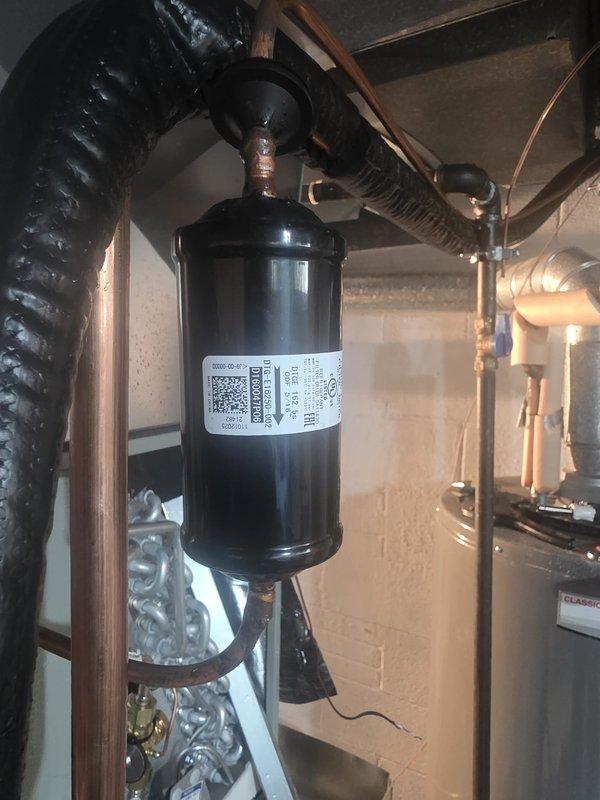 Completed full HVAC system installation including outdoor American Standard Silver Series condenser unit positioned and leveled against exterior brick wall with protective top cover installed. Interior work included installation of new filter-drier assembly with proper copper line connections, routing of flexible ductwork, and integration with existing mechanical systems in basement utility area. All components installed per manufacturer specifications with proper refrigerant line connections, secure mounting, and verified level placement of outdoor equipment.