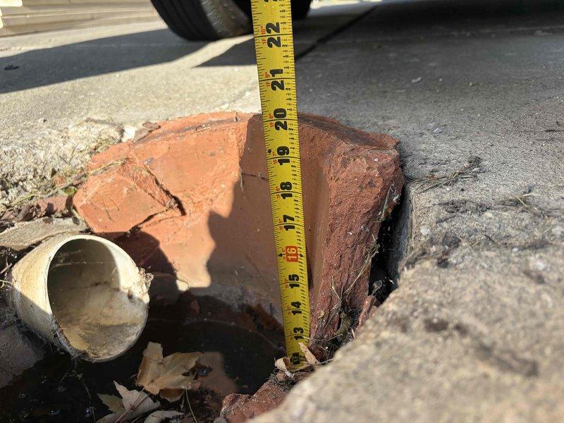 Conducted comprehensive assessment of deteriorated sewer drain crock system requiring replacement. Inspection revealed damaged terracotta clay pipe fragments and compromised subsurface infrastructure with significant pavement deterioration extending approximately 14-22 inches deep. Documented exposed PVC piping section showing angular displacement and interior residue accumulation. Secondary inspection identified corroded perforated metal drainage cover with extensive rust deterioration and open access point exposing interior plumbing components. Provided detailed photographic documentation of both street-level excavation site and interior floor drainage system to support replacement estimate for complete sewer drain crock assembly.