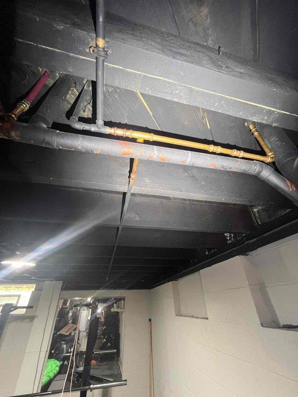 Responded to water leak originating from shower area affecting basement ceiling and home gym space below. Upon inspection, identified compromised plumbing connections in exposed ceiling piping system above workout area. Located source of leak in shower drain assembly with visible water damage to surrounding pipe connections and ceiling joists. Repaired faulty connections, sealed affected areas, and verified system integrity through pressure testing to ensure no further water intrusion into basement space.